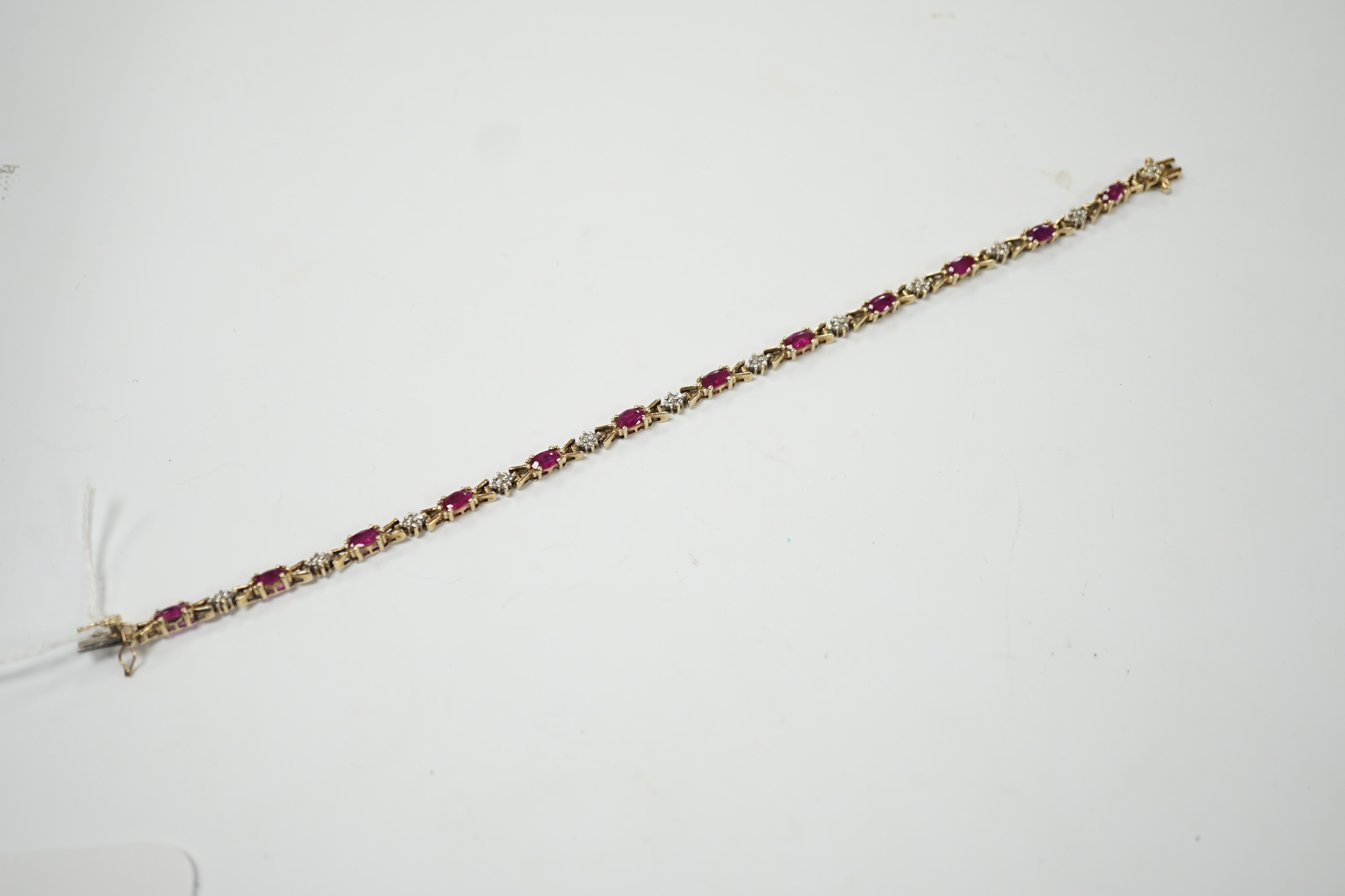 A modern 375 yellow metal, ruby and diamond cluster set line bracelet, 19cm, gross weight 7.6 grams. Fair condition.
